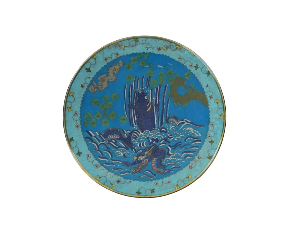 Un ancien plateau ou chargeur japonais décoratif en émail sur cuivre datant de la fin de l'ère Meiji. L'intérieur de l'assiette est orné d'un motif polychrome de poissons et d'un dragon de mer dans un paysage marin sur le fond bleu réalisé selon la