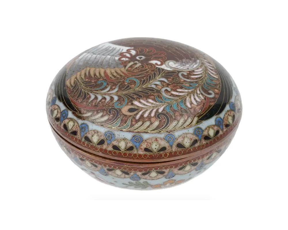 An antique Japanese, late Meiji era, covered enamel over brass jewelry or trinket box. The exterior of the ware is enameled with a polychrome image of a Phoenix bird, floral, foliage, geometrical patterns made in the Cloisonne technique. The base is