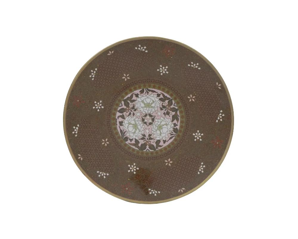 An antique Japanese enamel over copper plate or charger. The interior of the plate is adorned with a polychrome enamel medallion with blossoming Chrysanthemum flowers on the light pink ground surrounded by reticulated and floral ornaments made in