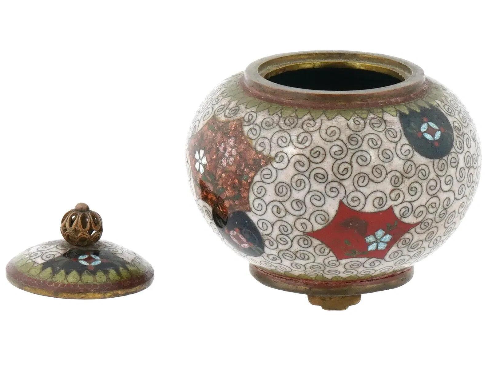 Antigua jarra japonesa con pie y tapa. Finales del periodo Meiji, antes de 1912. La jarra está recubierta de esmalte policromado con motivos florales y volutas. Levantado sobre tres patas. En la parte superior de la tapa hay un asa decorativa calada