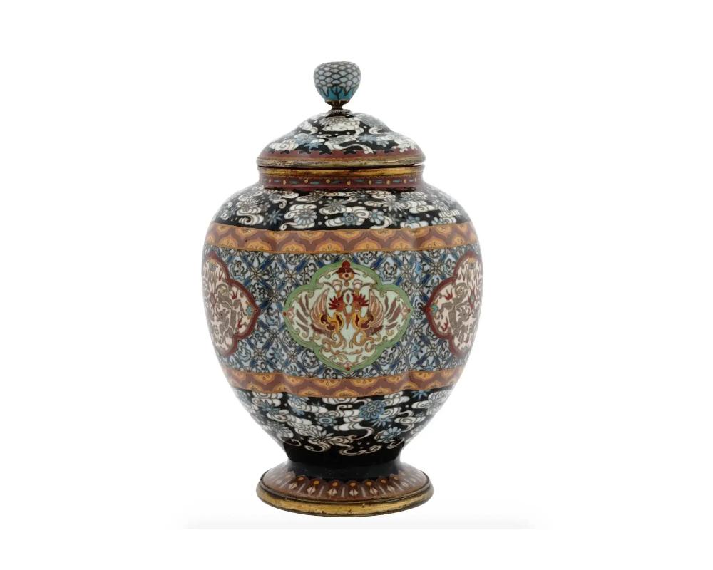 An antique Japanese cloisonne enamel lidded koro jar from the Meiji period standing on a foot and featuring traditional ornamentations to the center with two outer rims and stylized motifs on dark grounds coming to the shoulders and foot. The lid is