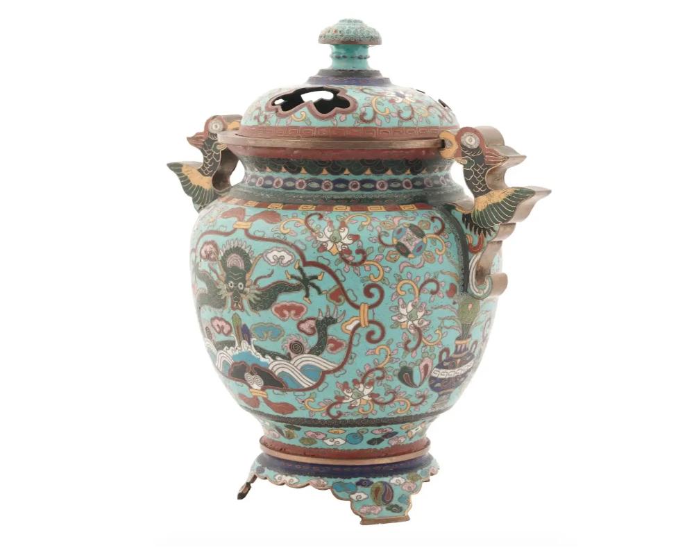 A fine antique Japanese lidded incense burner, made of brass and covered with polychrome cloisonne enamel patterns depicting traditional stylized floral motifs surrounding the central medallion depicting dragon flying in clouds. The body is flanked