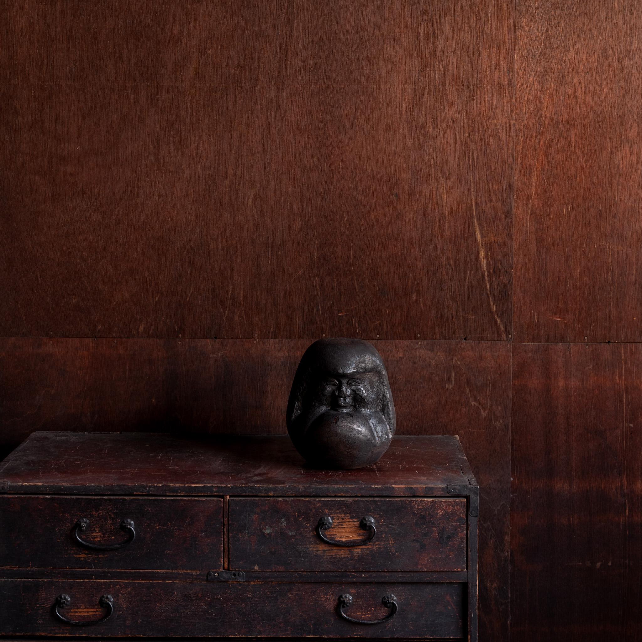 Eine beeindruckende handgeschnitzte Holzskulptur von Daruma. Die Figur ist aus einem dichten, dunklen Hartholz geschnitzt und zeigt ein ausdrucksstarkes Gesicht mit gerunzelten Brauen und meditativer Intensität - ein Symbol für Widerstandsfähigkeit