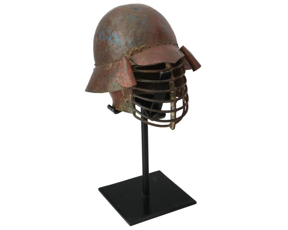 An antique Japanese iron samurai combat helmet, or Kabuto. Zunari type. Late Edo period, 19th century. Bowl-shaped helmet with a visor, solid neck guard, rod bars welded on the front. The item comes with a stand. Collectible Oriental Metalwork, Arms