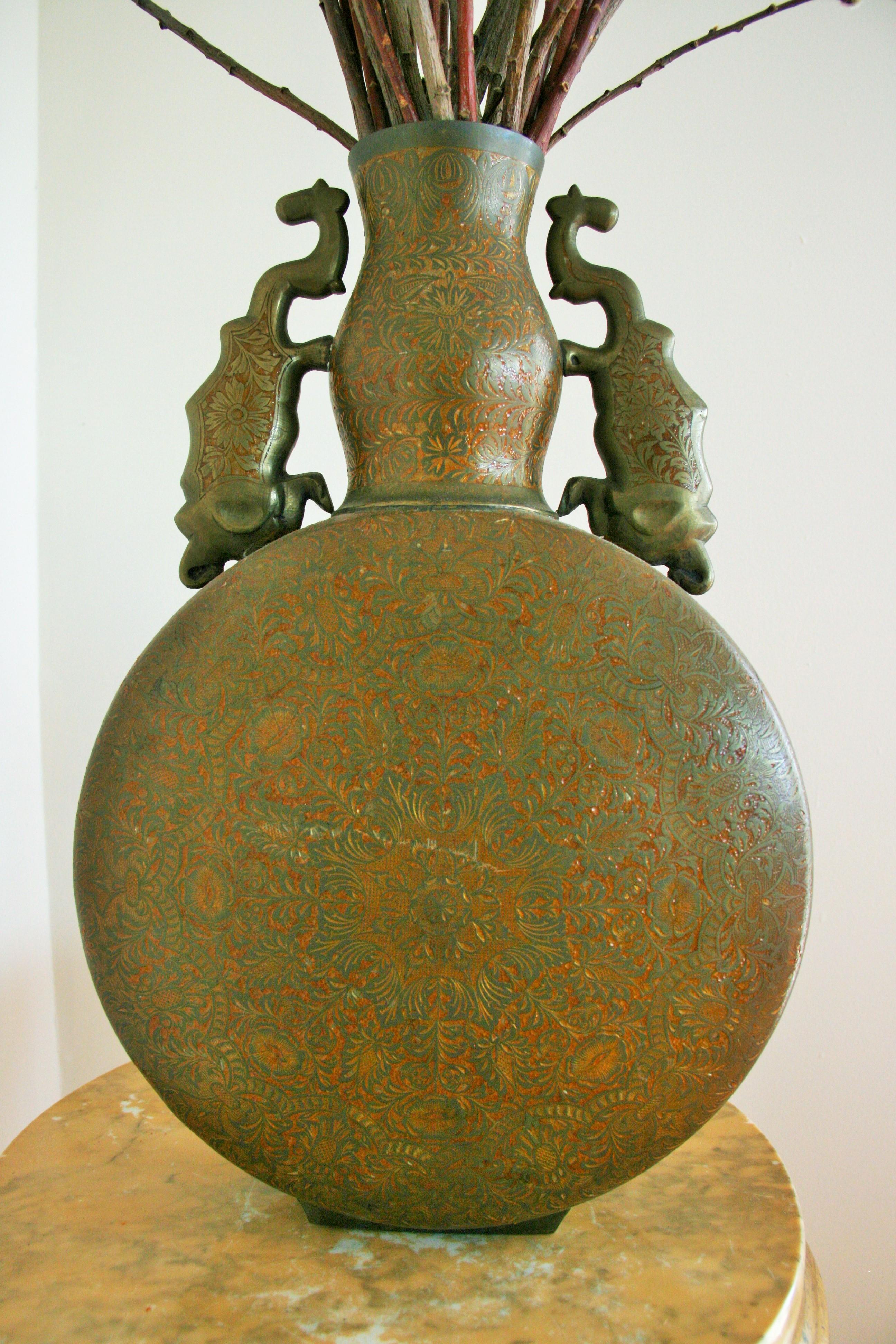 8-174 Embossed bronze  urn with stylized elephant handles
Bronze  has aged patina with red oxide impressions
Reeds not included.