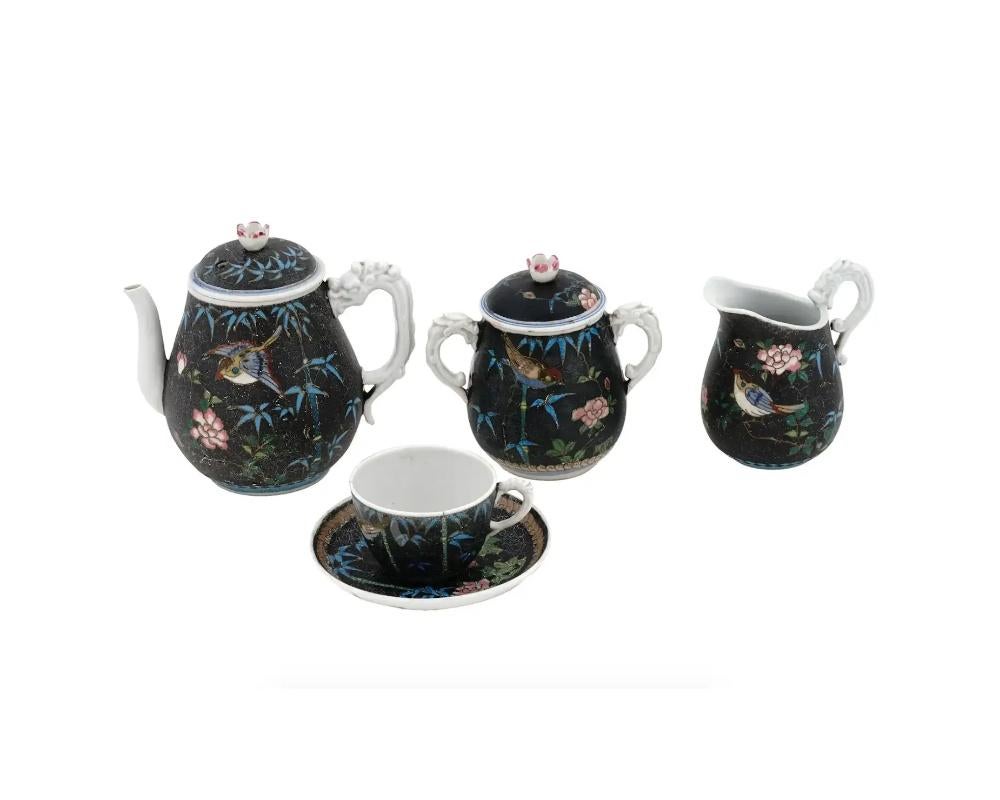 An antique Japanese enamel porcelain tea set. Features a captivating bird and floral design meticulously executed in the intricate cloisonne technique. The set includes a teapot, a lidded sugar bowl, a creamer, and a tea cup with saucer, each piece