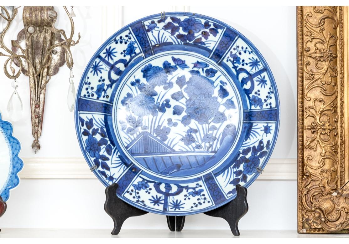 Chargeur ancien d'exportation japonaise bleu et blanc Arita. Le bord est divisé en six panneaux alternés et répétitifs contenant des pivoines avec des graminées ou des bambous en germination. Le centre avec réserve florale.
Marques de poterie sur