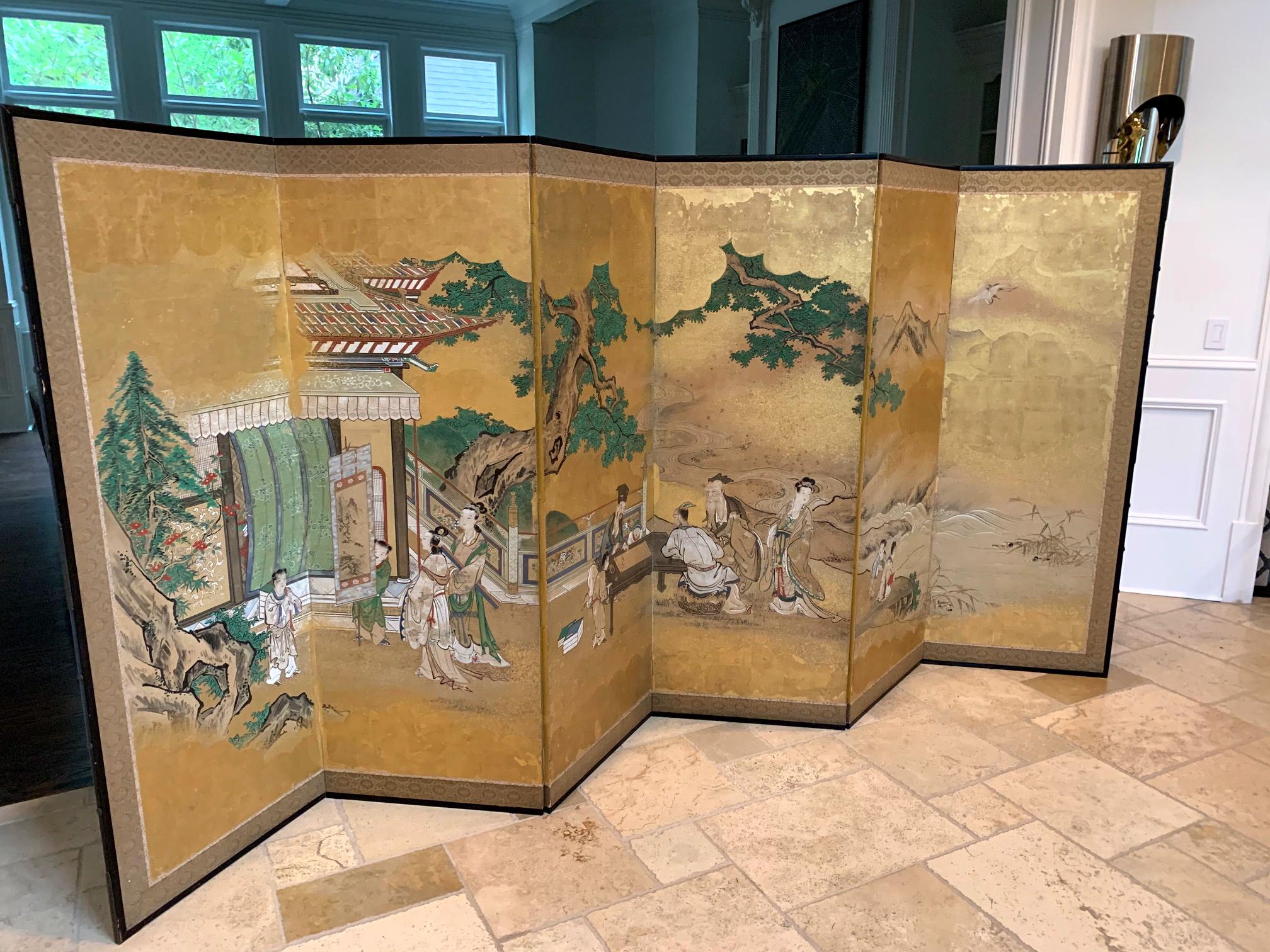 A Japanese floor screen with six folding panels in wood frames with brass hardware and gilt paper backing circa 18th century in Edo period. The screen depicts a Classic Chinese literary scene with groups of figures in the garden landscape setting.