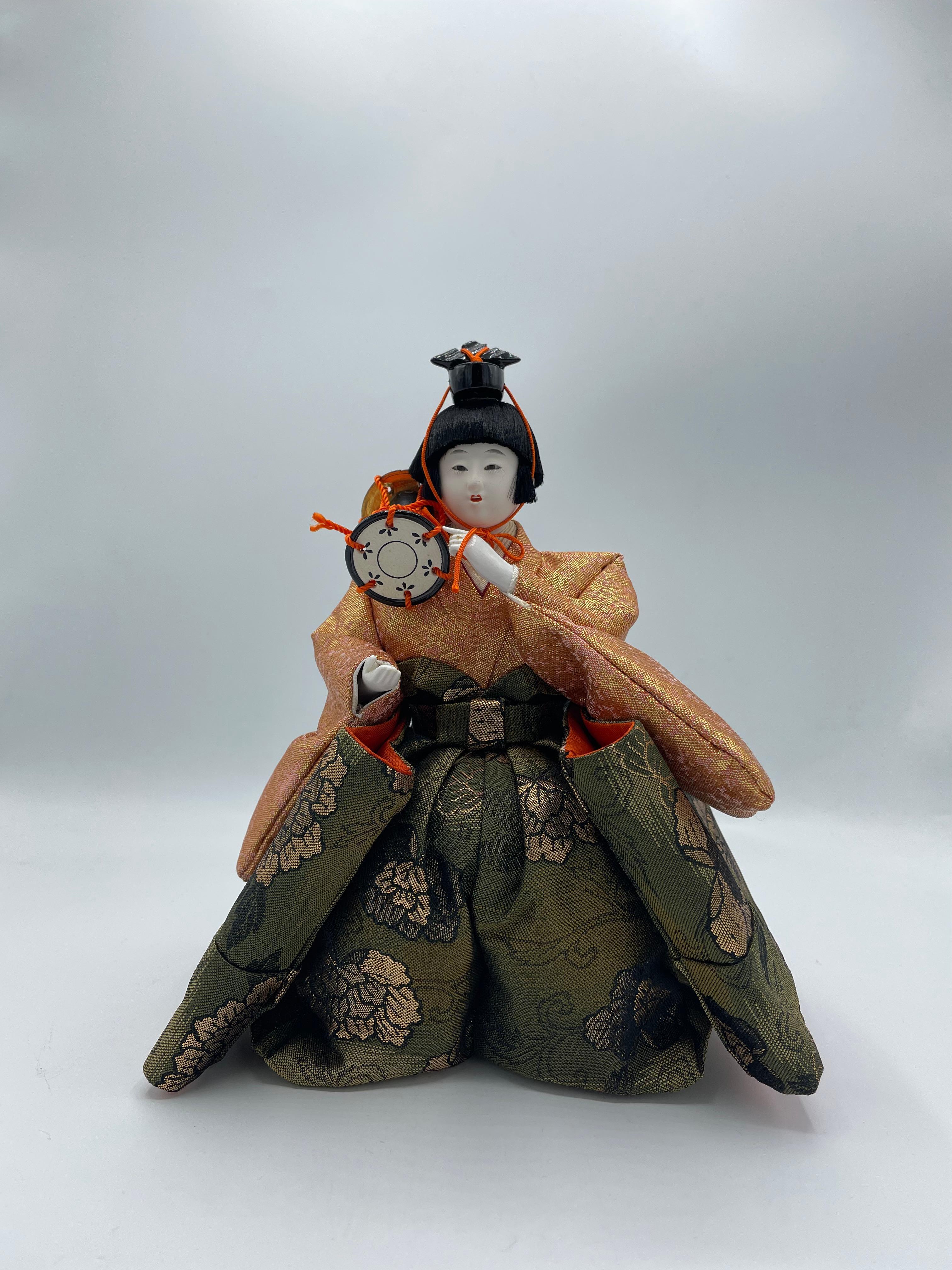 Il s'agit d'une poupée que nous utilisons pour le jour de Hinamatsuri. Cette personne est l'un des Goninbayashi.
Cette personne a un tambour. Cette poupée a été fabriquée avec du plastique, du coton et de la soie. Cette poupée a été fabriquée dans