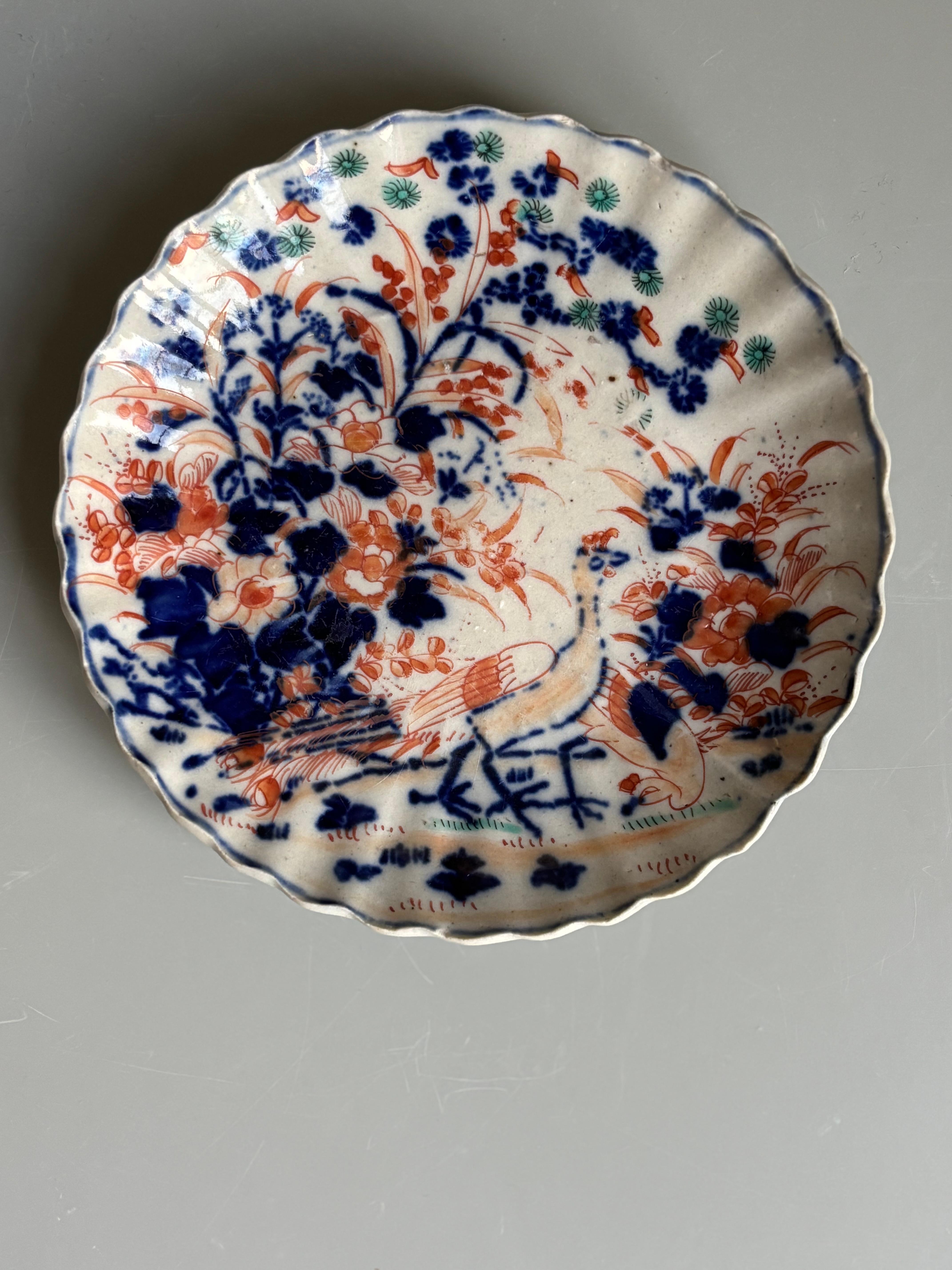 Early 19th century Japanese Imari porcelain vide-poche dish with hand painted floral decorations in the traditional Imari colors of cobalt blue and coral red with small green accents. Two peacocks are portrayed wandering along a small path in the