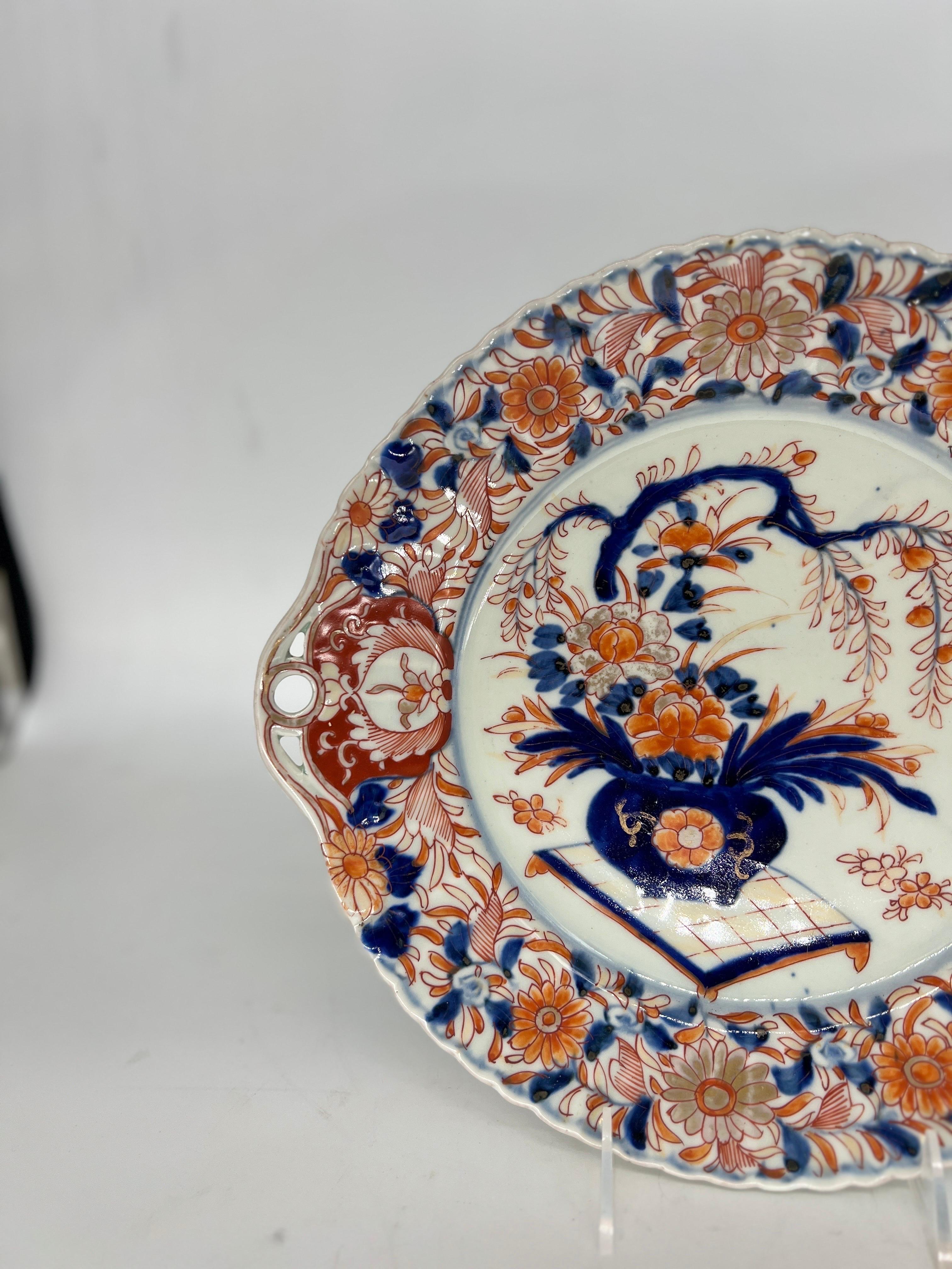 An antique Japanese porcelain Imari pattern platter. The platter is decorated with orange, red, blue and gold tone floral / foliate motifs to the edges. Which surround a central bonsai tree decoration to the center. Some would call the platter a