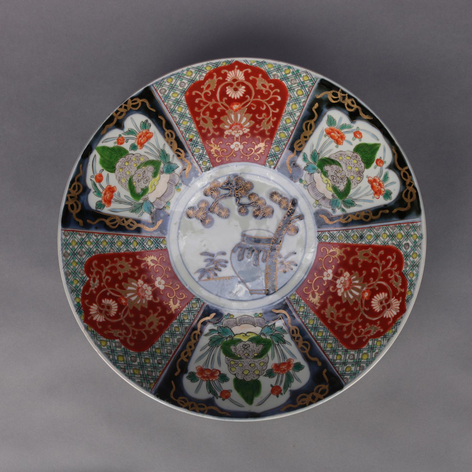 An antique Japanese Imari porcelain charger features hand painted panels of alternating garden scenes and scroll and foliate decoration surrounding central medallion with urn, gilt highlights throughout, en verso decoration, circa 1900.

***DELIVERY