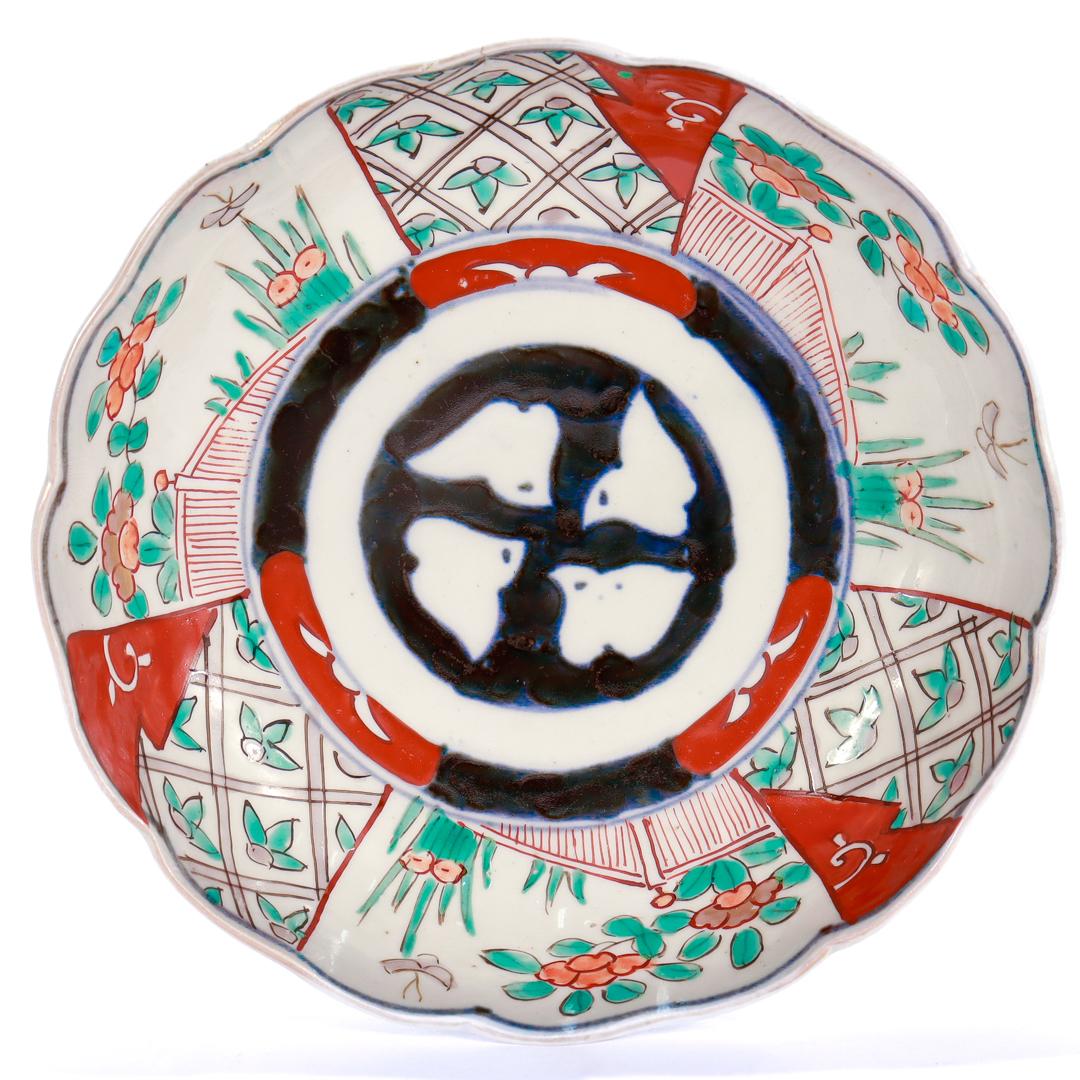 Eine feine antike japanische Imari-Porzellanschale.

Mit weißem Grund. Im Zentrum der Schale befindet sich ein stilisiertes Wappen des Shimazu-Klans (家紋, wörtlich: Familienwappen) in einem schwarz-roten Kreis, der von gemalten Blumenszenen umgeben