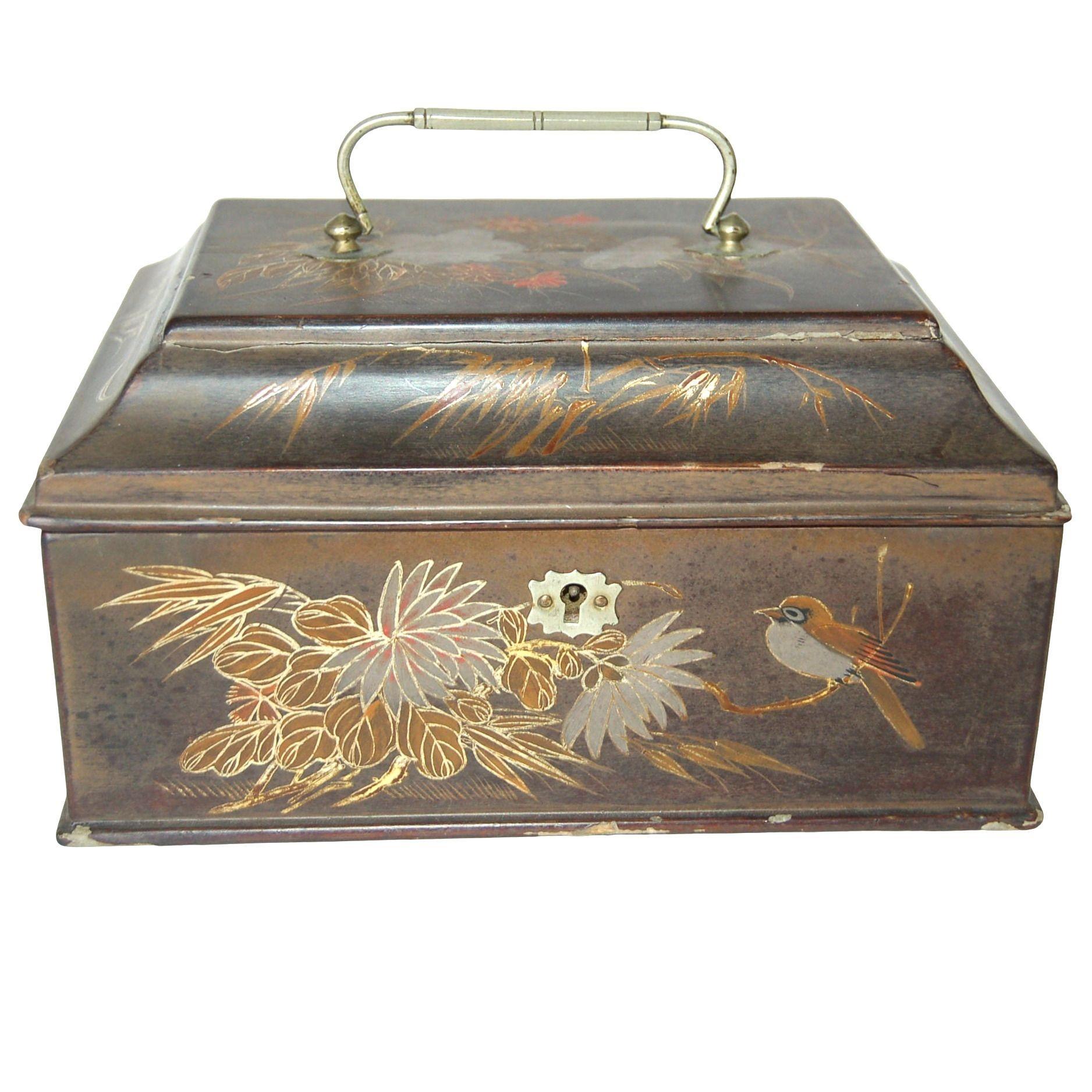 Un antiguo joyero japonés de metal, que representa un pájaro sobre una rama rodeado de follaje, encarna una refinada mezcla de arte y funcionalidad. La superficie exterior está intrincadamente pintada y muestra un pájaro bellamente detallado posado