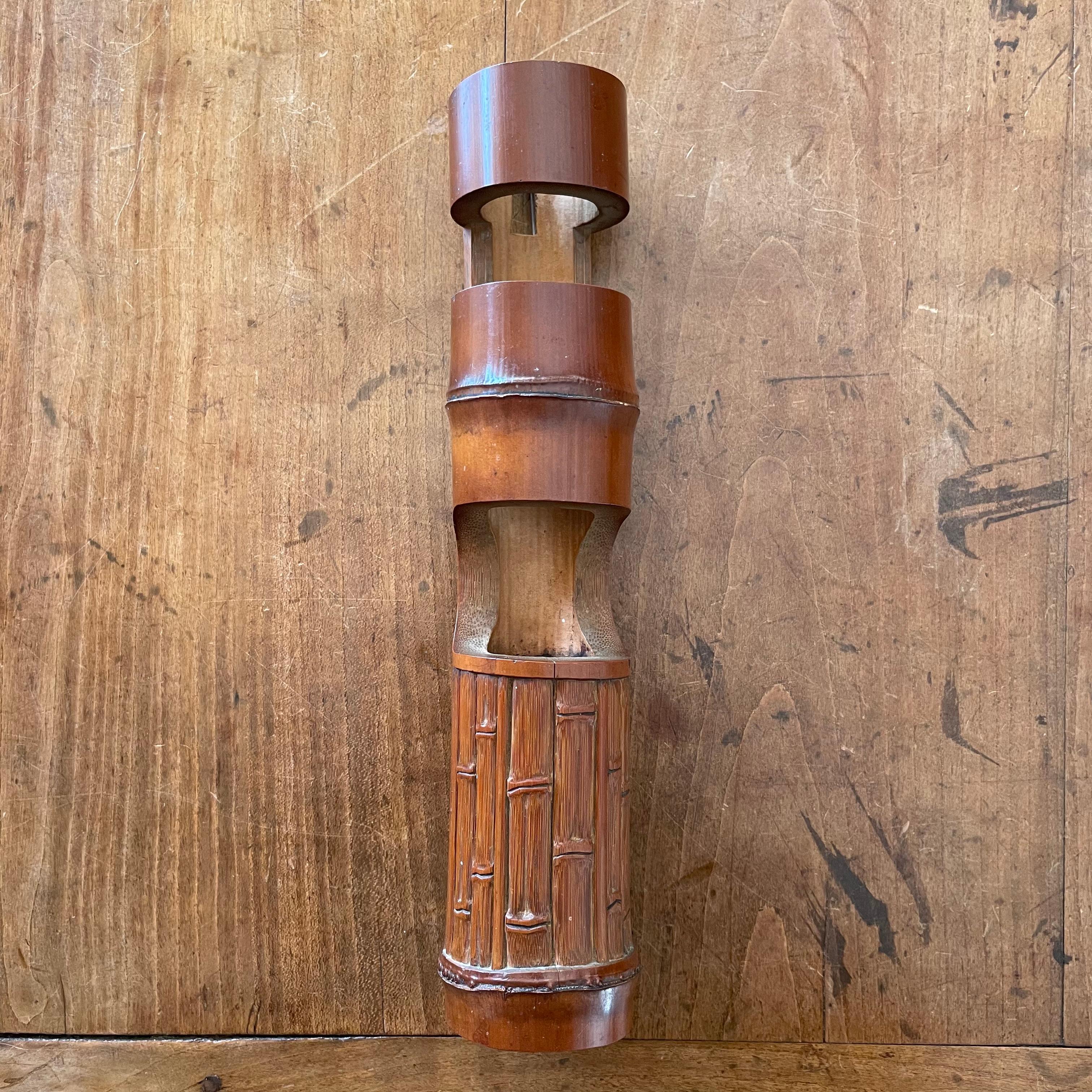 Japanese Kakehana (wall hanging vase) crafted of one thick segment of bamboo with two cutouts and front panel carved to resemble smaller segments of bamboo. Signature at the side. Excellent condition. 10.75 in. high. x 2 in. in diameter.(27.6 x 5