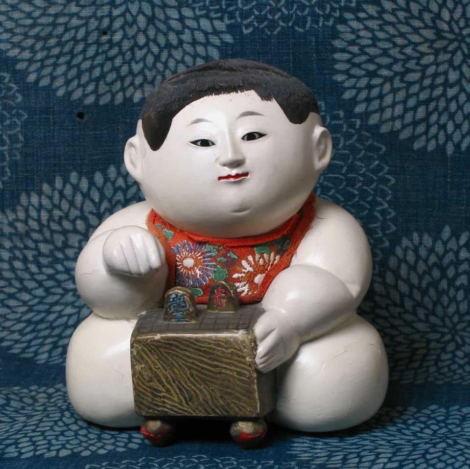 Japanese Kofuku-no-inori gosho ningyo (a good luck wish palace doll) of a plump male child kneeling with a game board in front of him, traditionally given amongst the nobility as a wish for good fortune in gambling endeavors and competitions, all