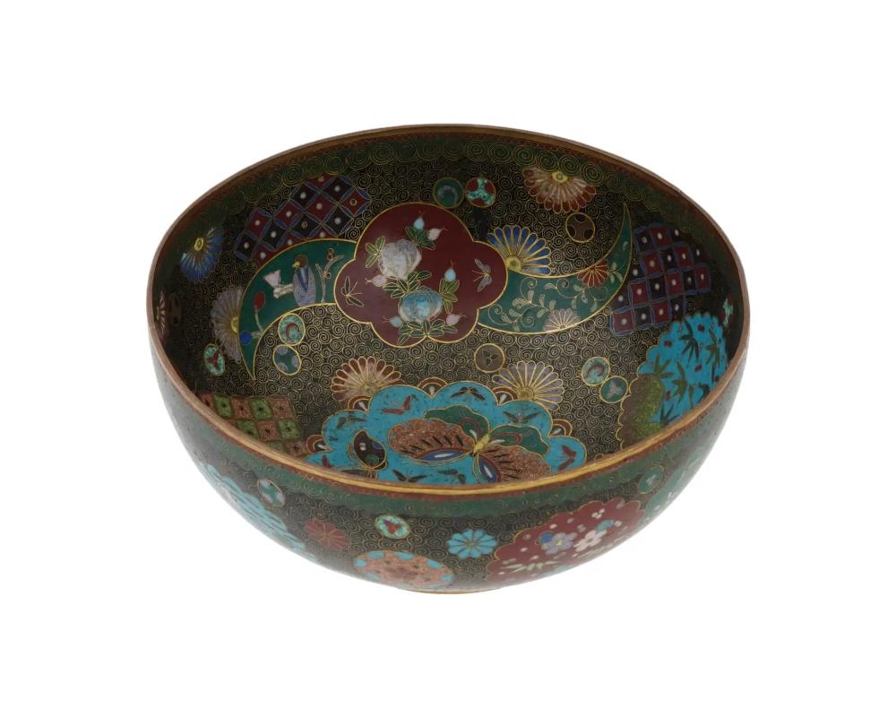 An antique Japanese Meiji era Kyoto School enamel over brass bowl. Circa: late 19th century to early 20th century. The bowl is enameled with polychrome medallions depicting blossoming flowers, butterflies, and a human figure in a garden surrounded