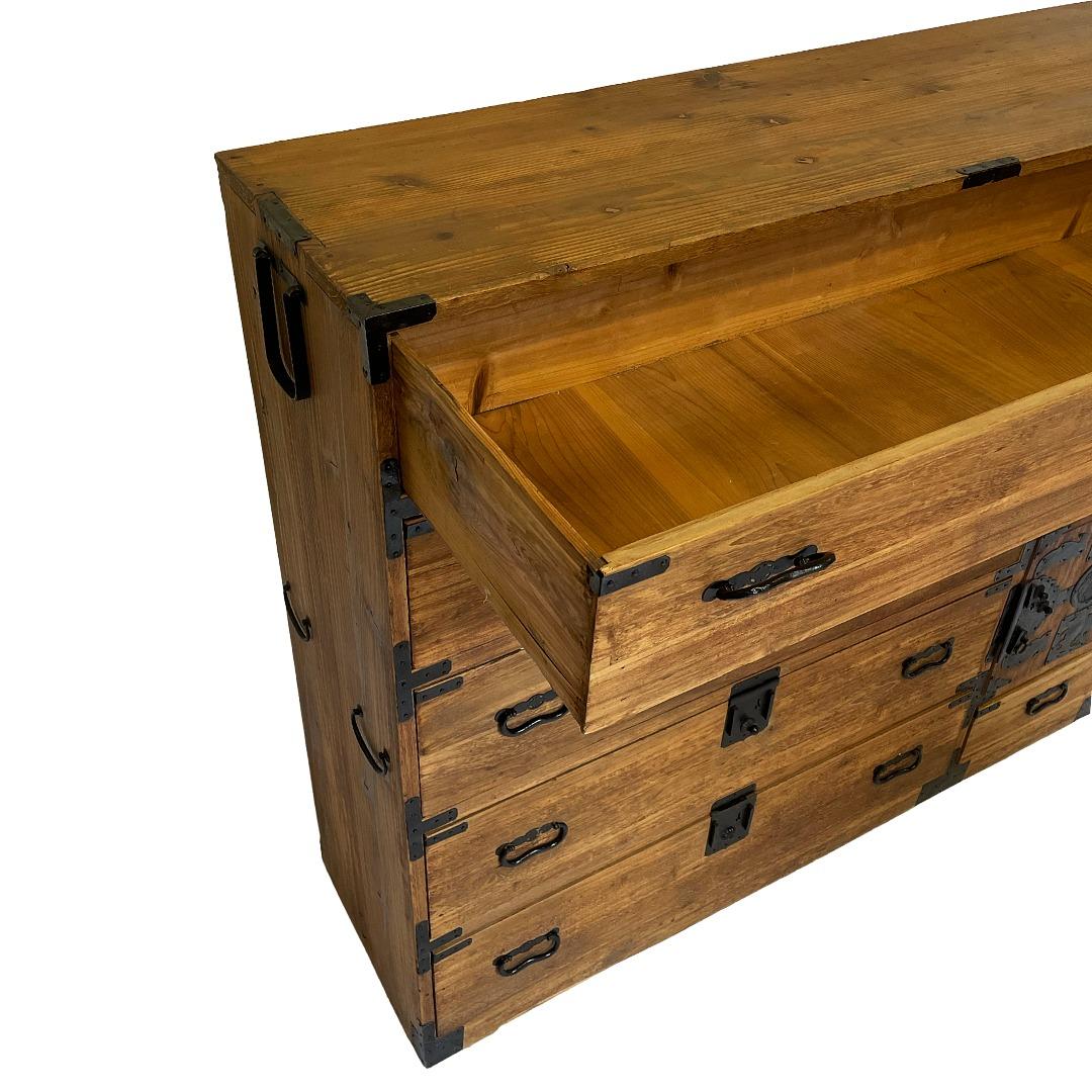 Un'eccezionale cassapanca a due sezioni proveniente dalla regione di Kyushu, realizzata in legno massiccio di kiri (paulownia) con una patina calda e consumata dal tempo che mette in risalto le sue venature sottili. Mantenendo la ferramenta