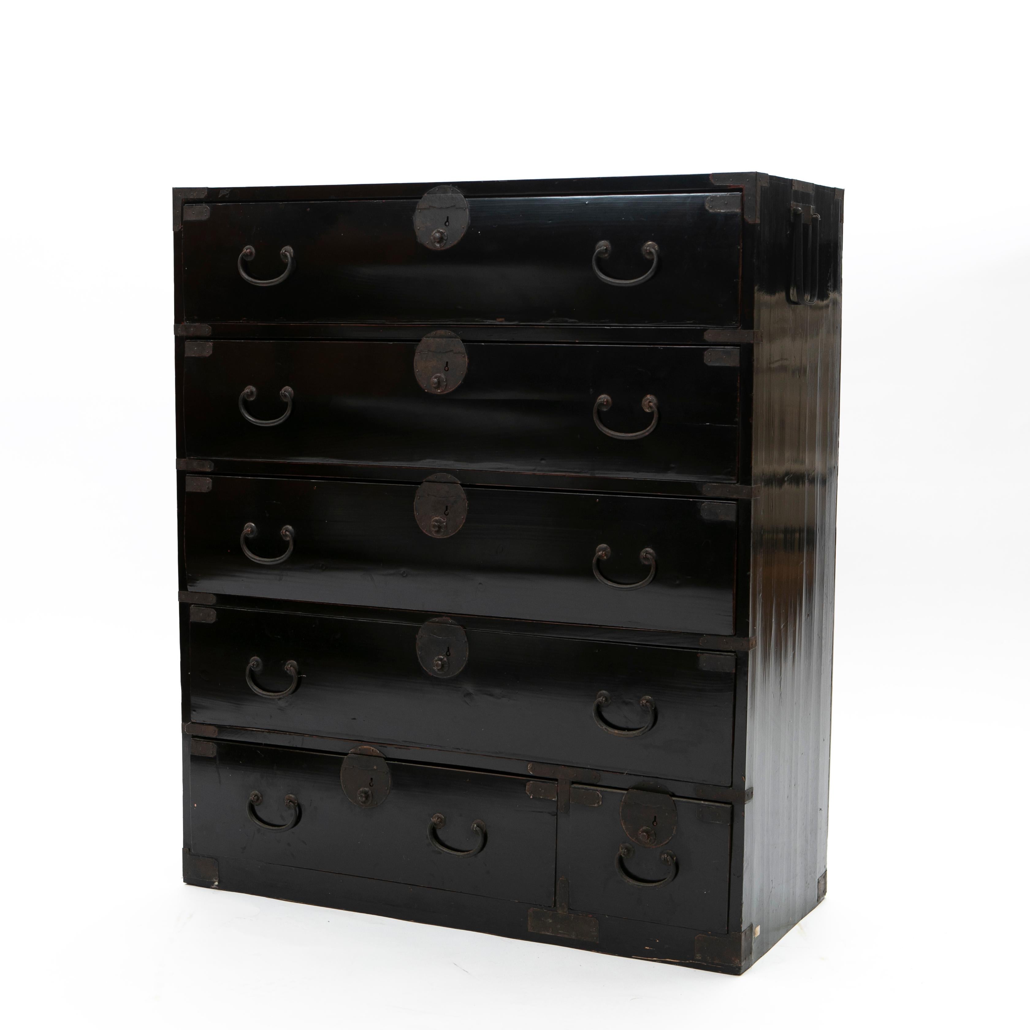 A Japanese Meiji period six drawer tansu chest. 
This façade showcases four large drawers followed by a medium and a smaller one placed in the lower section.

Black lacquered pine wood fitted with original iron handles and hardware. Carrying handles