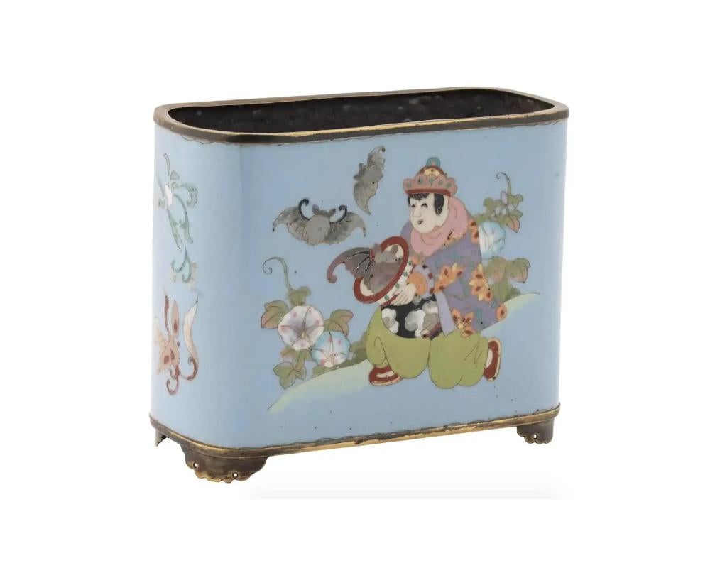 An antique Japanese Meiji period brass brush pot of rectangular form decorated with a cloisonne enamel figure of a man holding a bowl with bats, and images of birds and flowers to the body. Stands on four feet. Circa the early 20th century. Antique
