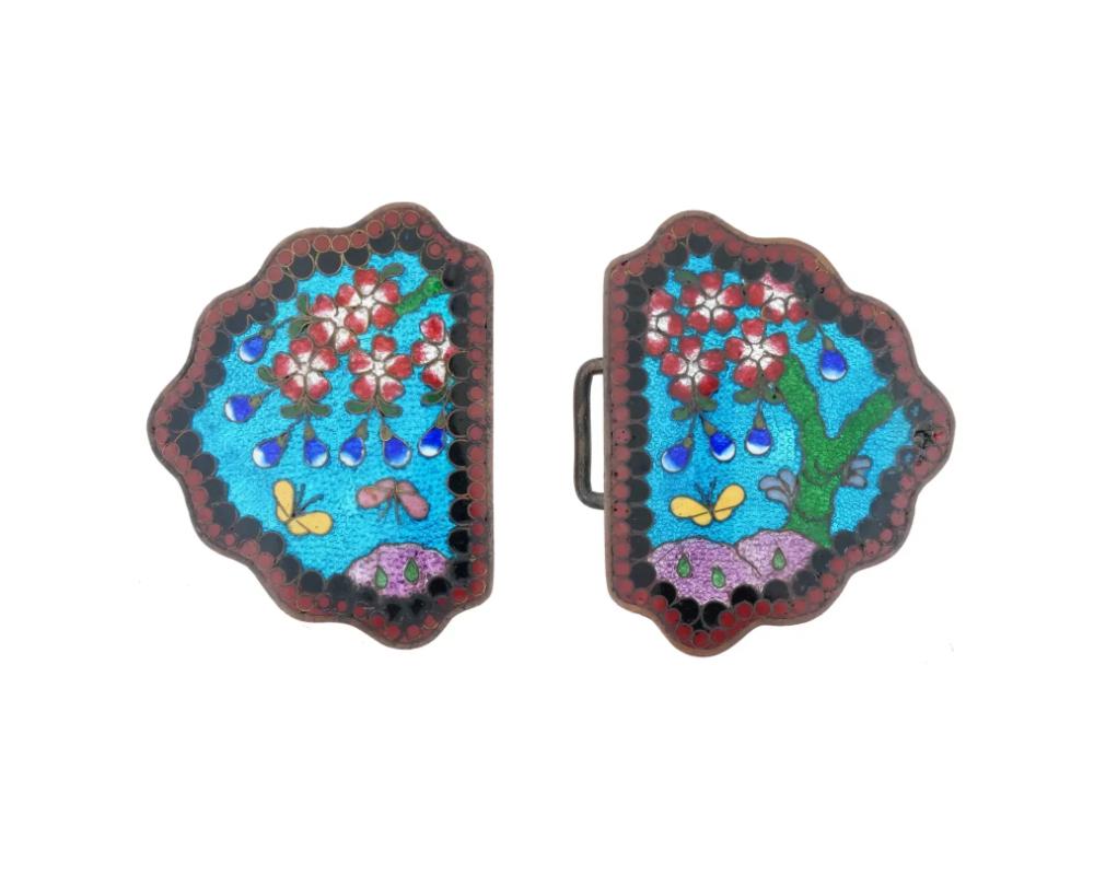 An antique Japanese, late Meiji era, enamel over copper belt buckle. The ware consists of two parts with a clasp. The belt buckle is covered with polychrome enamel floral, foliage and butterfly motifs surrounded by a geometrical ornament on the