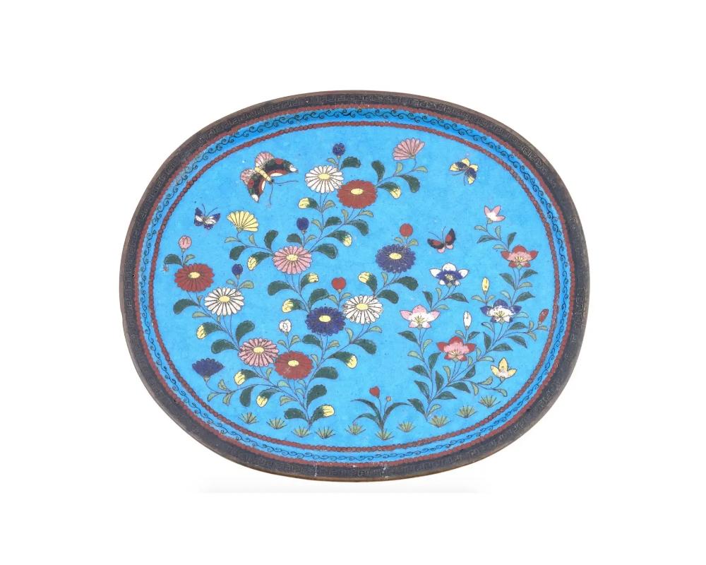 An antique Japanese, late Meiji era, footed enamel over brass tray. circa: late 19th century to early 20th century. The tray is adorned with polychrome images of blossoming flowers and butterflies on turquoise ground made in the Cloisonne technique.
