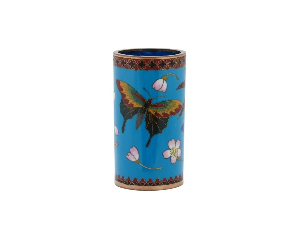 An antique Japanese Meiji Era enamel over copper brush pot. Circa: late 19th century to early 20th century. The cylindrical form pot is enameled with polychrome images of butterflies, flowers, and leaves made in the Cloisonne technique on a