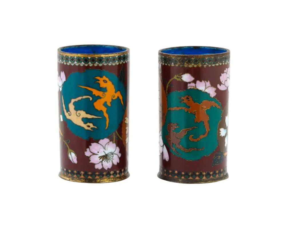 A pair of antique Japanese copper brush pots with cloisonne enamel design. Late Meiji era, before 1912. Cylinder shape. The items are decorated with cherry blossoms and abstract ornaments against the red background. The interior is cobalt blue.