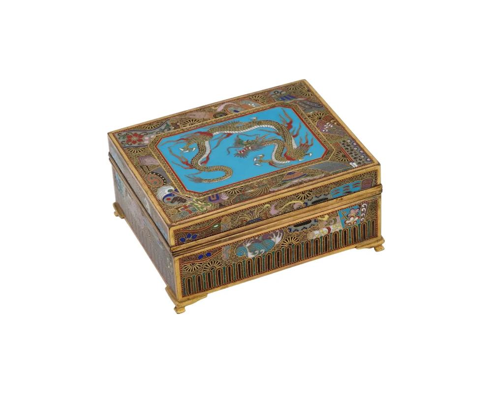 An antique Japanese copper trinket box with cloisonne enamel design. Late Meiji era, before 1912. Footed rectangular piece. Black and red ground colors, polychrome floral ornaments. The lid is garnished with a dragon panel, the bottom depicts