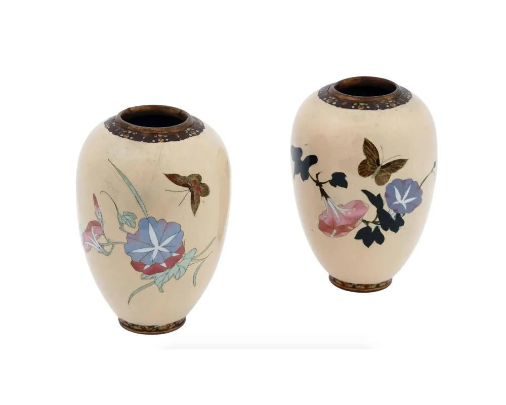 An antique Japanese cloisonne enamel vase from the Meiji period featuring an elegant form with high shoulders and light beige ground color. Decorated with multicolor floral and foliate motifs with butterfly images to the body. A rim and base are