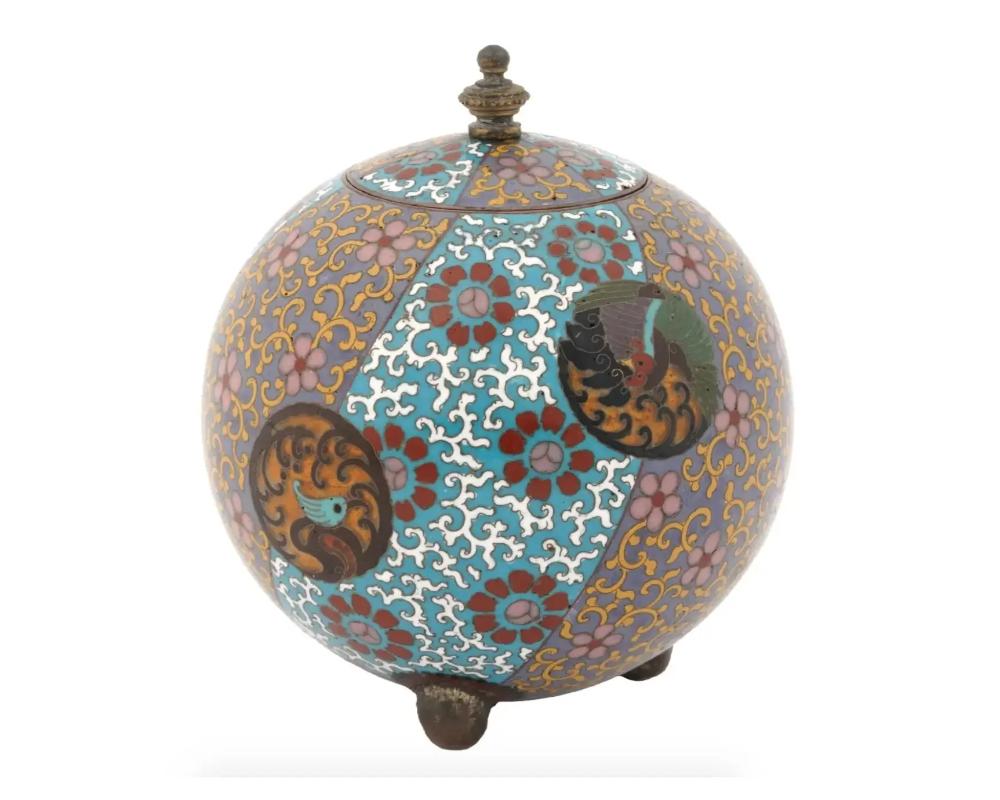 An antique Japanese Meiji period lidded jar decorated with cloisonne enamel shield shaped panels with Hoho birds. The tea jar is of rounded shape standing raised on three shaped small brass feet and with a recessed cover with a flower finial. Circa