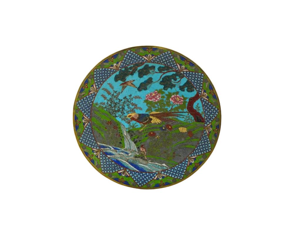 An antique Japanese early Meiji era enamel over copper charger plate. The exterior of the plate is adorned with a polychrome scene with birds in a river landscape with blossoming flowers and plants on a turquoise ground made in the Cloisonne