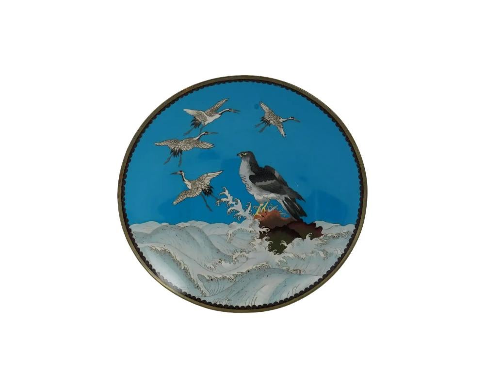 An antique Japanese Meiji era enamel over copper charger plate. The exterior of the plate is adorned with a polychrome scene with an eagle standing on a rock and cranes flying over waves on a turquoise ground made in the Cloisonne technique. The