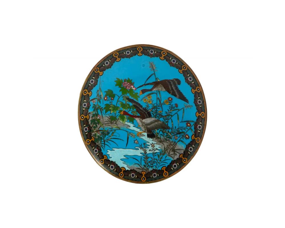 An antique Japanese, probably Goto school, enamel over copper charger plate. The exterior of the plate is adorned with a polychrome image of ducks flying over a pond with blossoming flowers and plants on a turquoise ground made in the Cloisonne