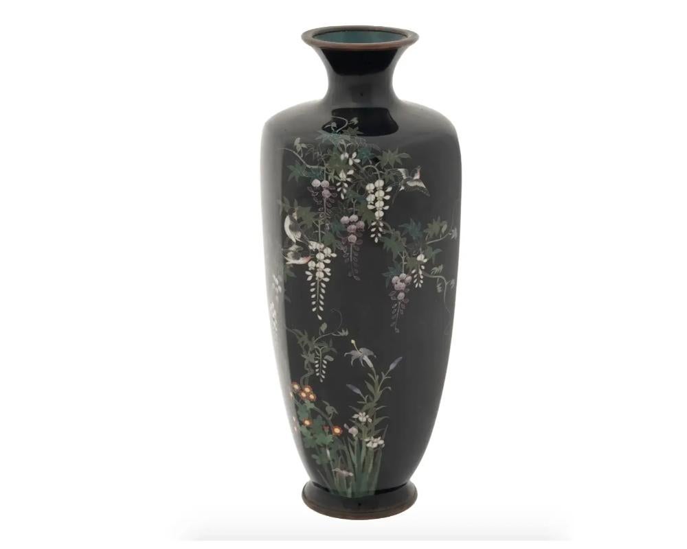 An antique Japanese Meiji Era brass and enamel vase. Circa: early 20th century. The vase is enameled with polychrome images of birds and Wisteria flowering plants made in the Cloisonne technique on a black ground. Unmarked. Antique and Vintage Asian