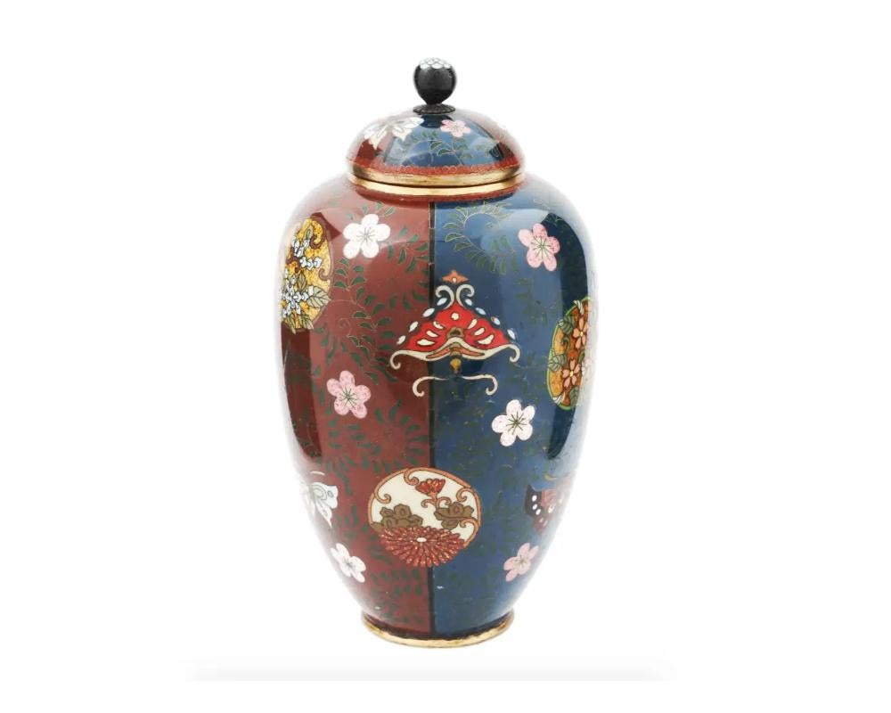 An antique Japanese Meiji era covered amphora shaped enamel over brass urn vase. The exterior of the vase is adorned with polychrome enameled continuous design of overlapping stylized floral roundels, scrolling vines, and butterflies scattered over