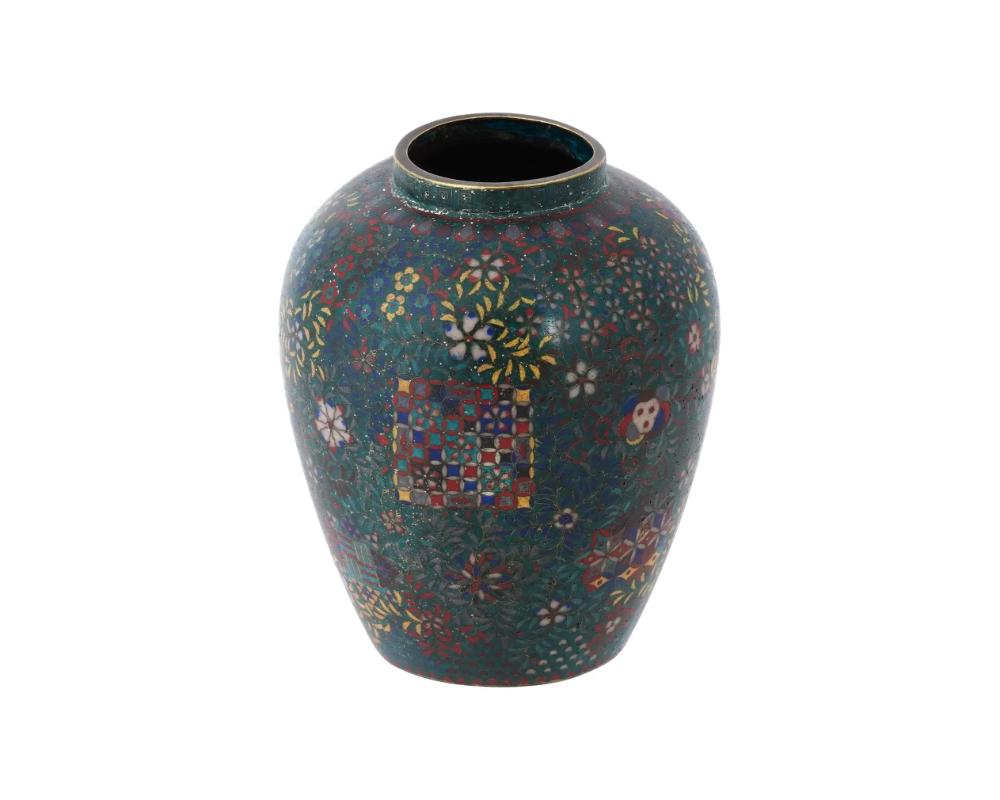 An antique Japanese, Meiji era, enamel over copper vase. The vase has an urn shaped body and a wide neck. The ware is enameled with polychrome floral, foliage, geometrical, and reticulated ornaments on the dark green ground made in the Cloisonne