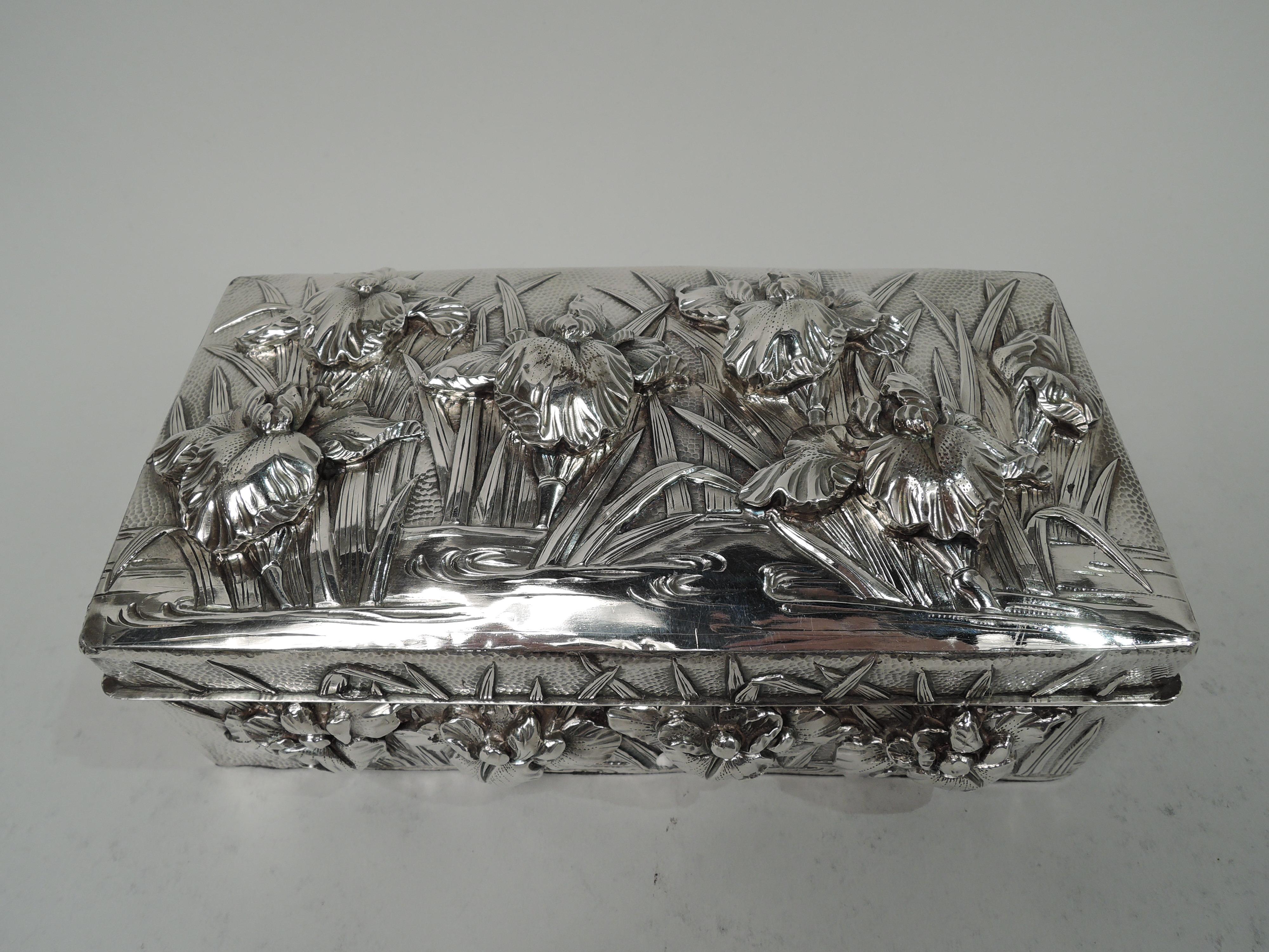 Japanese silver box, ca 1890. Rectangular with straight sides and hinged cover. On cover top and box sides are high-relief iris flowers and tendrils in eddying water. Stippled ground. Box and cover interior lined with stained wood. Open