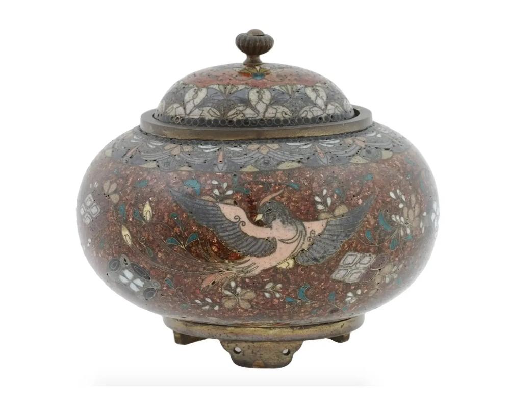 An antique Japanese, late Meiji Era, lidded and footed enamel over brass censer koro or jar. Circa: late 19th century to early 20th century. The sphere form jar is enameled with images of Phoenix birds, surrounded by floral and foliage motifs made
