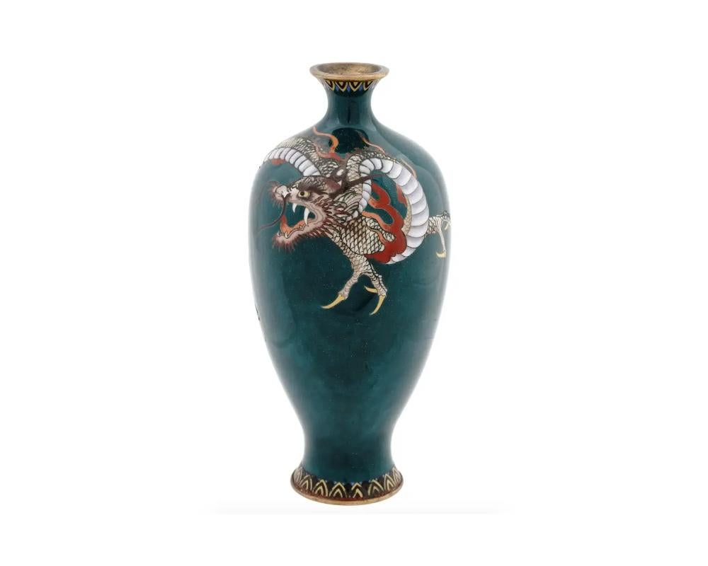An antique Japanese late Meiji era enamel over brass vase. The amphora shaped vase with a narrow fluted neck. The vase is adorned with a polychrome image of a dragon made in the Cloisonne technique. The base and the neck are adorned with a foliage