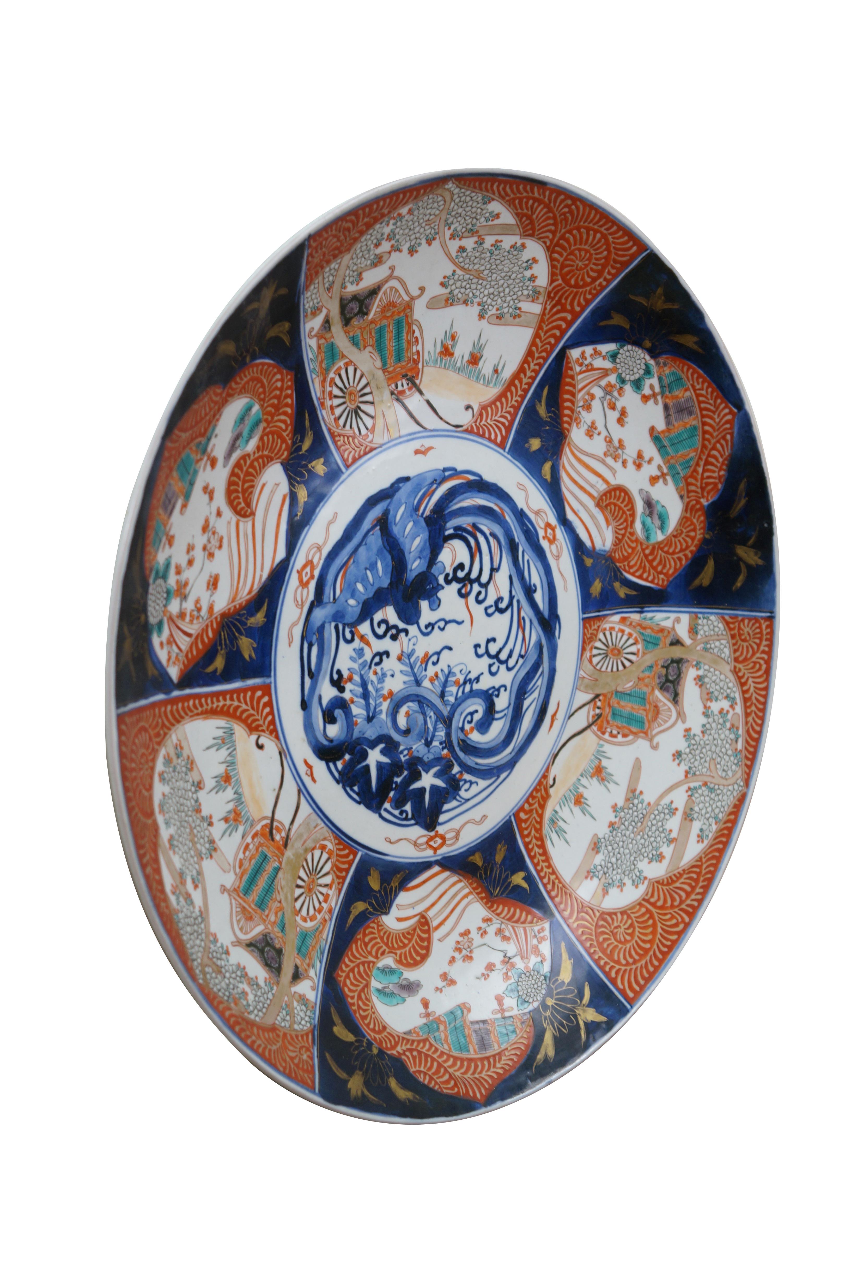 Antique Japanese imari porcelain platter / charger, decorated in blue, orange, green and gold with alternating panels of a hand drawn carriage / rickshaw and flower trimmed window screens, around a central motif of a flying phoenix / dragon.