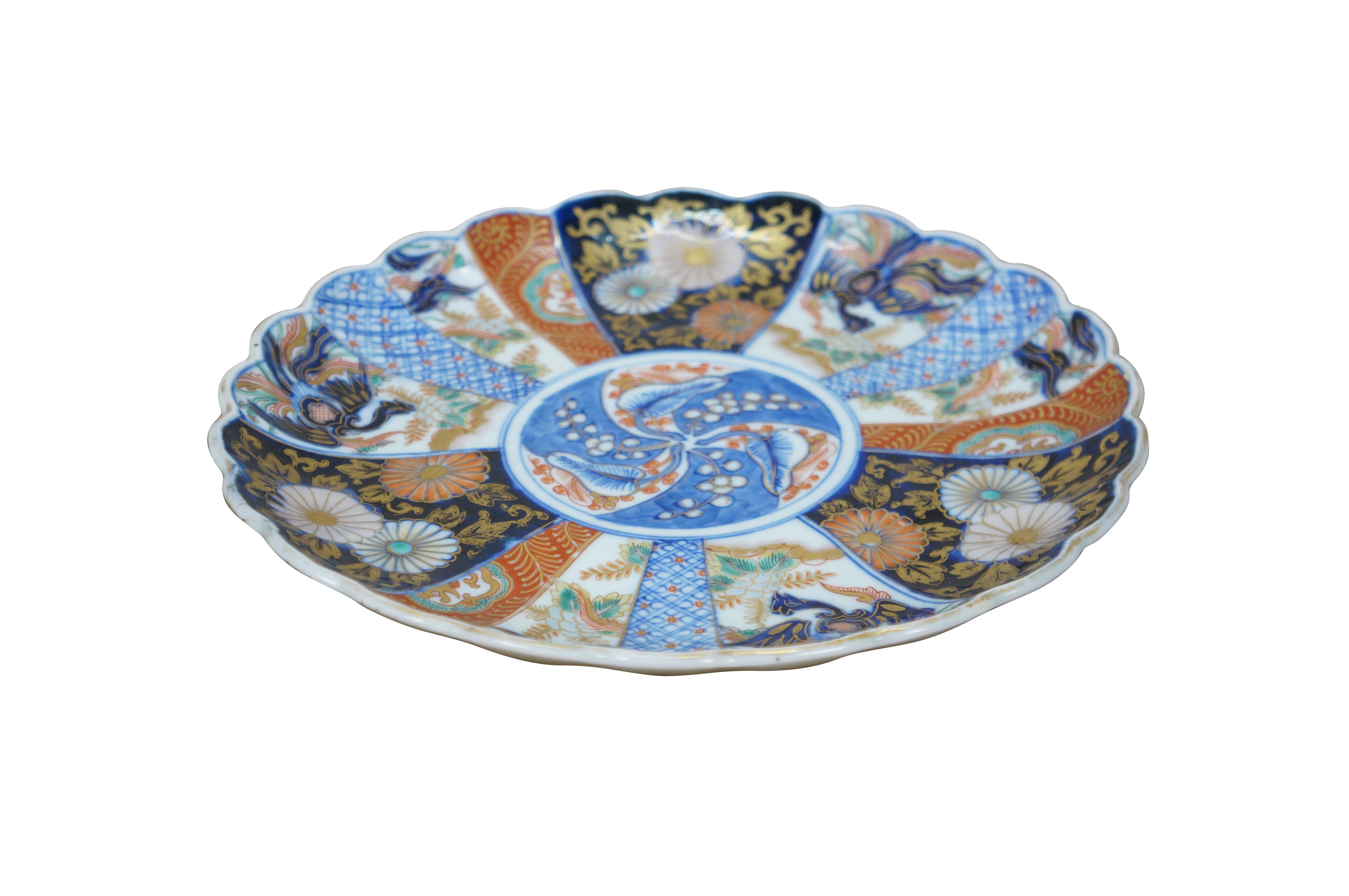 Ancien plat de service / chargeur en porcelaine japonaise imari à bord festonné, décoré en bleu cobalt, orange, or et vert d'un motif central de baies et de feuilles, entouré de panneaux de fleurs, de feuillages et d'un oiseau phénix en