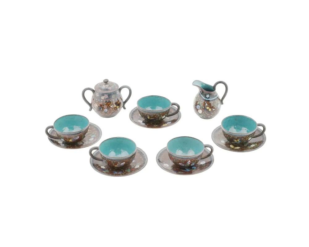 An antique Japanese Meiji period enamel tea set adorned with intricate floral patterns.Consisting of five cups, five saucers, a creamer, and a lidded sugar bowl, it showcases the traditional Japanese technique of cloisonne, where fine wires are used