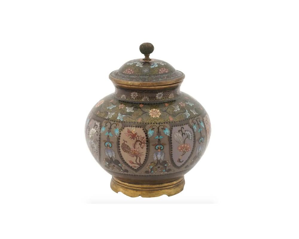 An antique Japanese Meiji period lidded jar decorated with cloisonne enamel flowering shrub patterns.

The jar of rounded bulbous shape stands on a narrow round foot with a raised narrow neck and hat shaped cover with a raised finial. Circa late