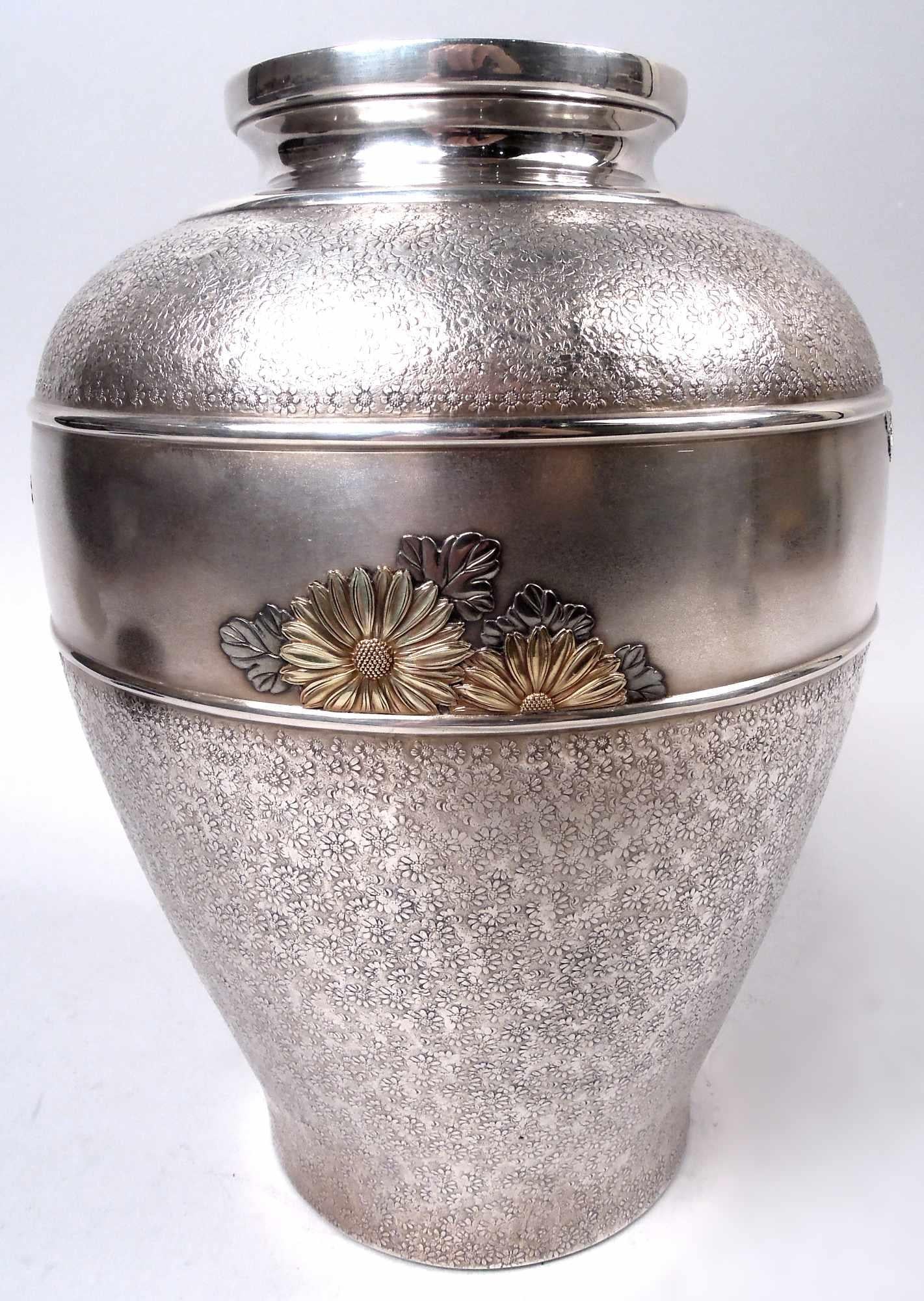 Vaso giapponese in argento Meiji, 1890 circa. Ovoidale con collo corto e liscio. Terreno denso e in basso rilievo di margherite. Sulla spalla fascia rifinita alla maggiordomo con la stessa in oro e argento colorato applicata alla fascia superiore e