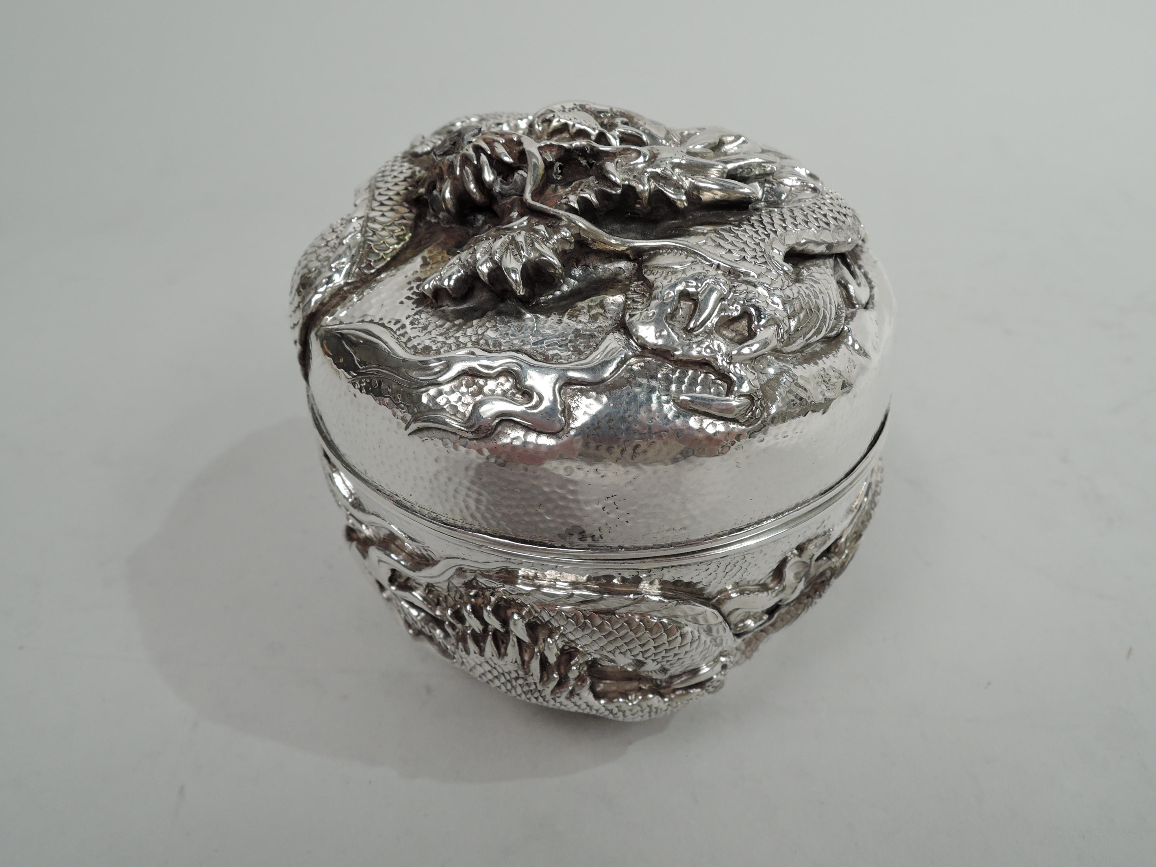 Japanese Meiji silver box, circa 1890. Round; gently curved sides applied with wraparound dragon—a scaly, spikey beast that chases its tail. A second coiled on cover top. Spot-hammered ground. Double walled. Japanese marks and stamp for Kuhn &
