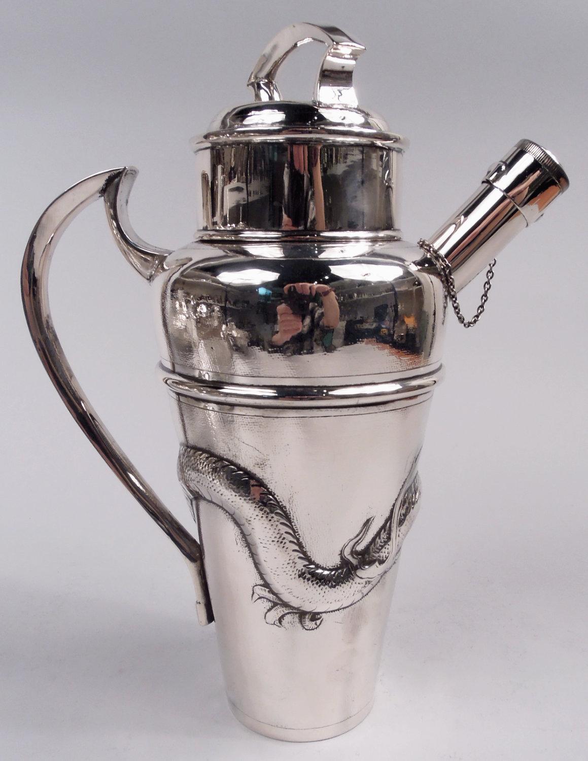 Chinese export silver cocktail shaker, ca 1910. Tapering and girdled bowl with curved shoulder, high-looping handle, and stubby spout with chained cap. Cork-lined cover with scroll-bracket handle. Wraparound tail-chasing dragon with horns and fangs