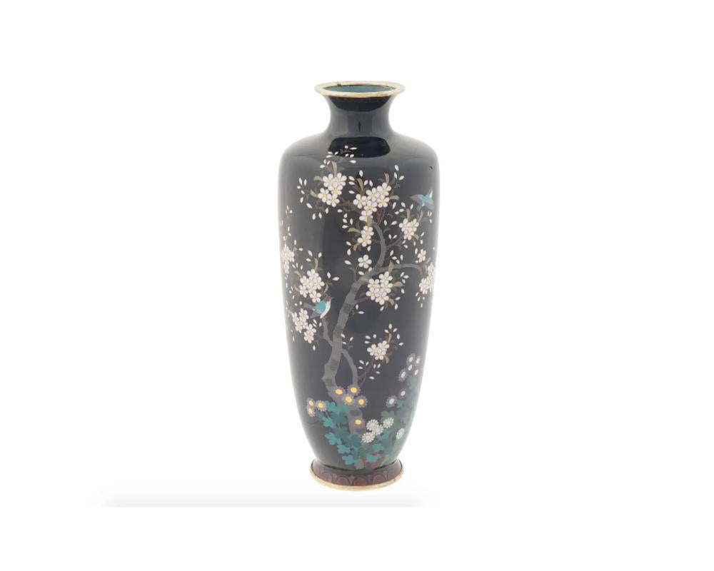 An antique Japanese Meiji period cloisonne vase of a baluster shaped body rising from a slightly spreading foot to a broad waisted neck and everted rim, decorated with a flowering tree and plants worked in silver wire and enamels, set against a blue