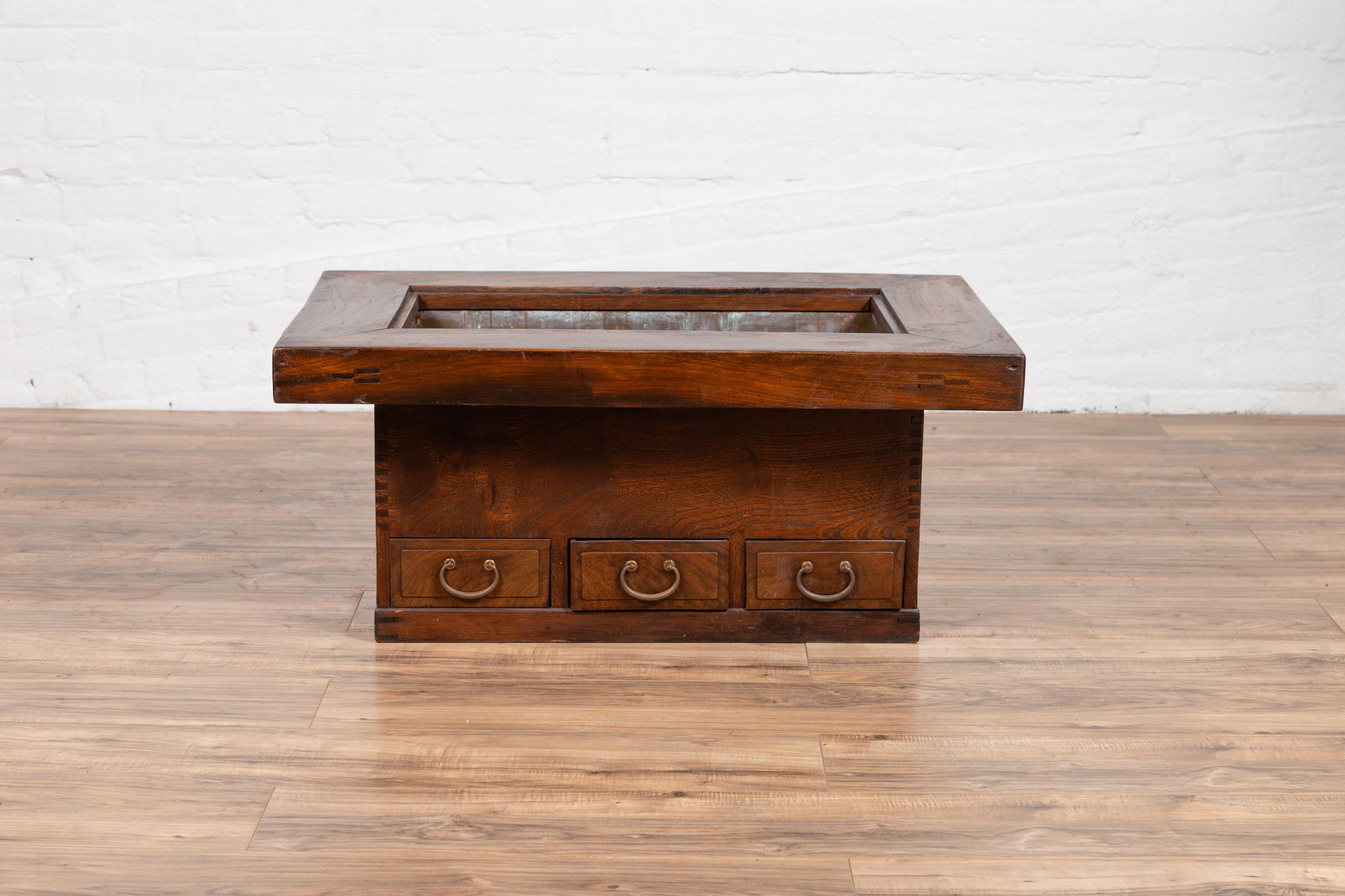 An antique 19th century Japanese rectangular keyaki wood hibachi from the Meiji period, with copper liner and three drawers. Used for cooking or warming sake or tea, this elegant hibachi features a rectangular frame surrounding the central opening