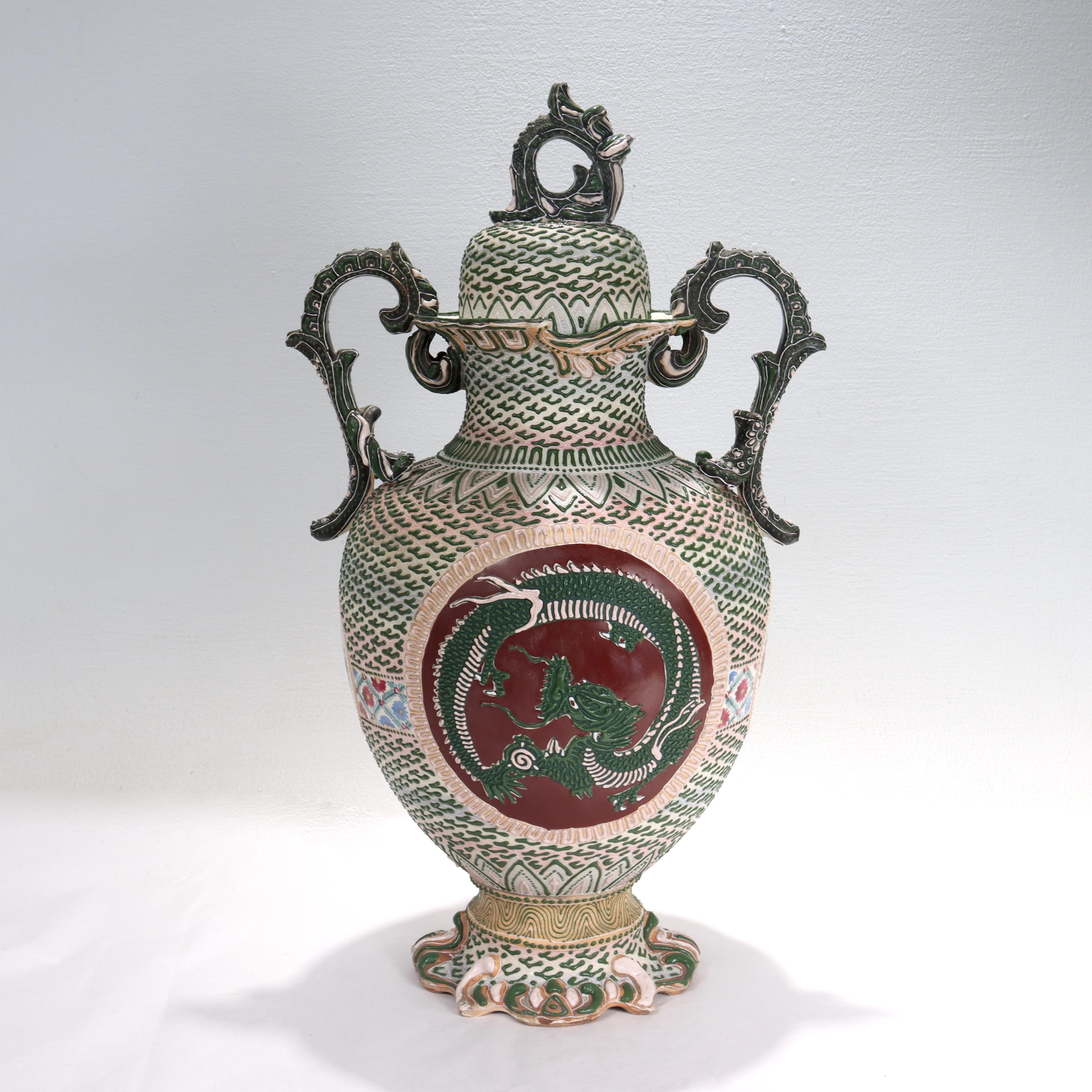 A fine antique Japanese Nippon porcelain vase or covered urn.

With green, pink, and white tones in raised moriage enamel that gives a three-dimensional effect. 

Decorated with 4 cartouches throughout. The main cartouche features a moriage dragon